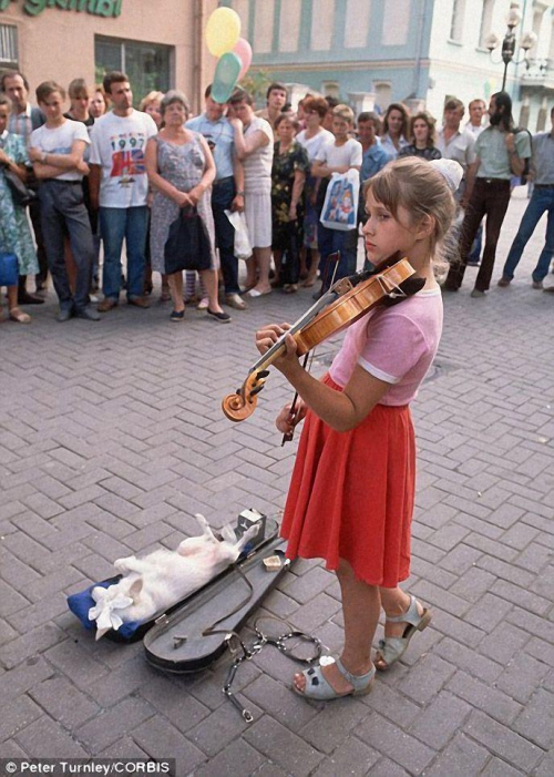 Девочка играет на скрипке перед толпой, а ее собака развалилась в футляре для скрипки на улице Арбат в Москве.