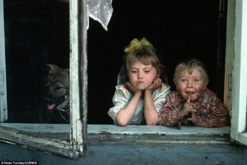 Двое грязных детишек выглядывают из окна в горно-металлургическом городке в Сибири.
