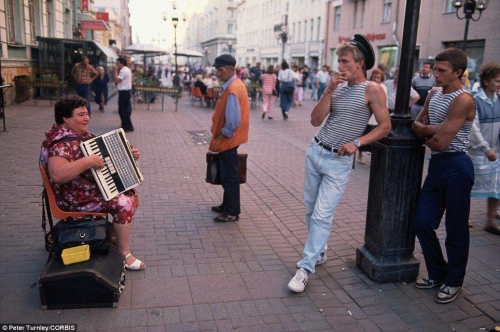 Женщина играет на аккордеоне на популярной пешеходной улице Арбат в Москве, а несколько стоящих мужчин ее слушают.